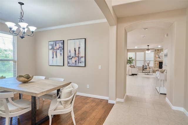 dining area featuring a fireplace, ornamental molding, ceiling fan with notable chandelier, and light wood-type flooring