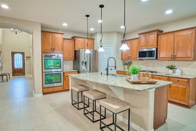 kitchen featuring stainless steel appliances, light stone counters, a center island with sink, and sink