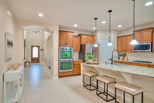 kitchen featuring light stone countertops, sink, backsplash, a breakfast bar area, and appliances with stainless steel finishes