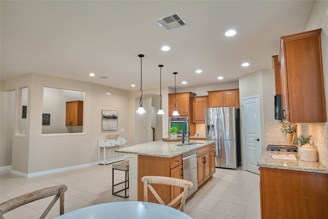 kitchen featuring light stone countertops, appliances with stainless steel finishes, tasteful backsplash, a kitchen island with sink, and pendant lighting