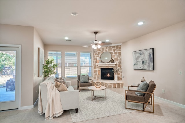 living room featuring ceiling fan, a stone fireplace, light tile patterned floors, and a wealth of natural light