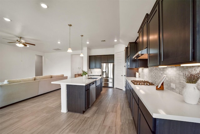 kitchen with appliances with stainless steel finishes, tasteful backsplash, sink, a center island with sink, and hanging light fixtures