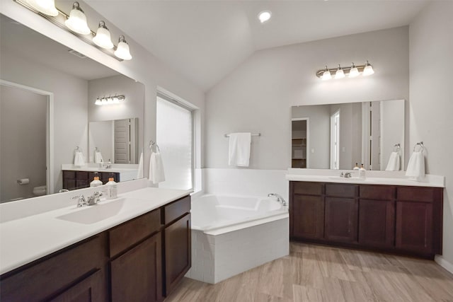 bathroom featuring vanity, toilet, tiled bath, and vaulted ceiling