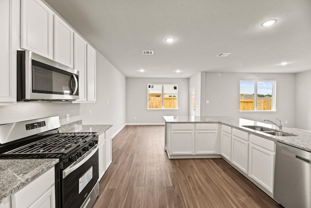 kitchen with light stone countertops, appliances with stainless steel finishes, dark hardwood / wood-style flooring, sink, and white cabinetry