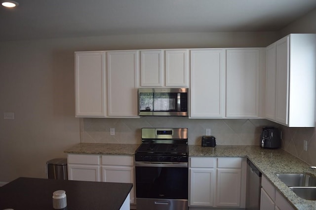 kitchen with sink, stainless steel appliances, tasteful backsplash, light stone counters, and white cabinets