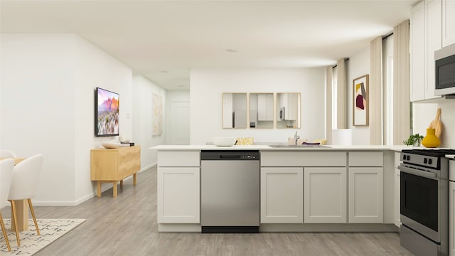 kitchen featuring kitchen peninsula, stainless steel appliances, sink, light hardwood / wood-style flooring, and white cabinetry