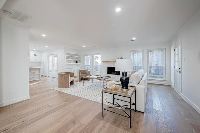 living room featuring built in features, french doors, light hardwood / wood-style floors, and a brick fireplace