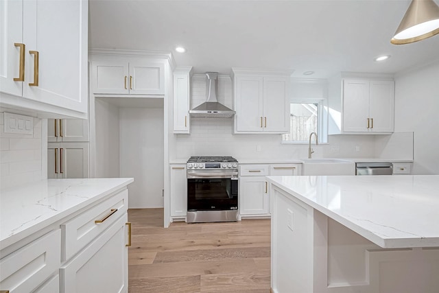 kitchen featuring wall chimney range hood, light hardwood / wood-style flooring, appliances with stainless steel finishes, light stone counters, and white cabinetry