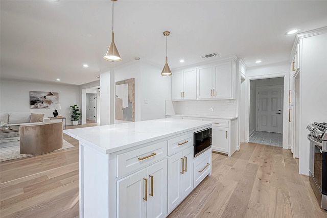 kitchen with white cabinetry, black microwave, stainless steel gas stove, hanging light fixtures, and light hardwood / wood-style floors