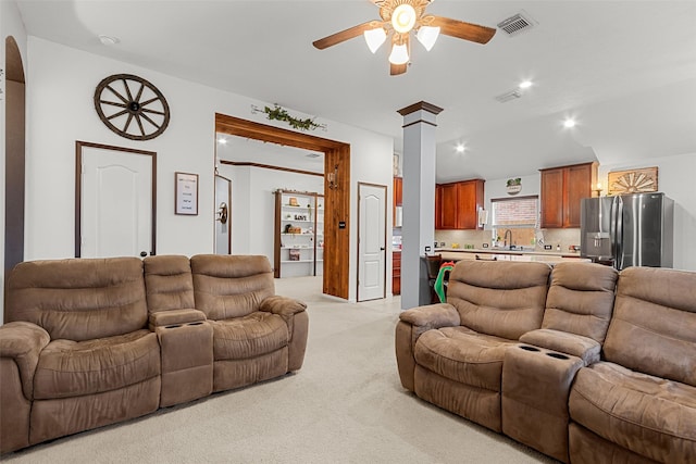 carpeted living room featuring ornate columns, ceiling fan, and sink