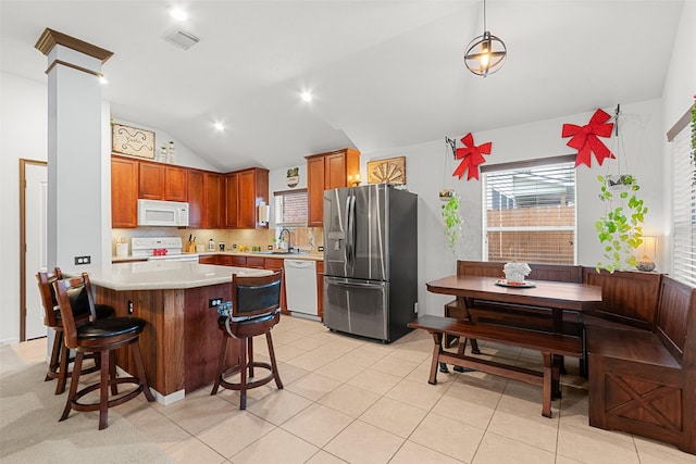 kitchen with white appliances, vaulted ceiling, sink, pendant lighting, and a breakfast bar area