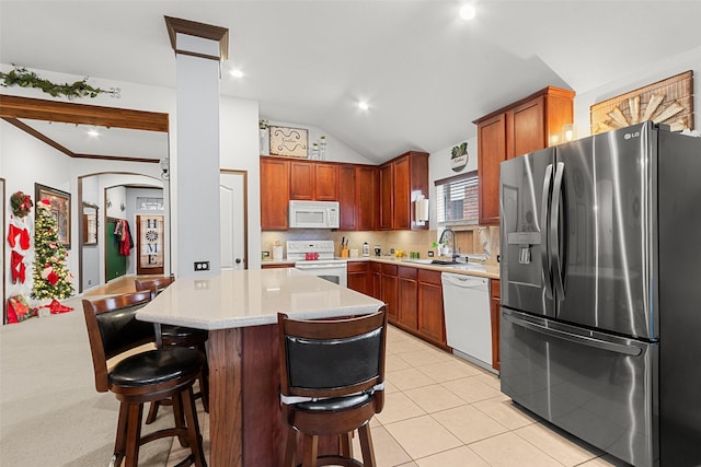 kitchen with a kitchen breakfast bar, white appliances, light colored carpet, vaulted ceiling, and a center island