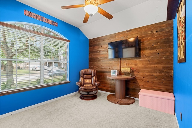 sitting room featuring carpet flooring, ceiling fan, wooden walls, and vaulted ceiling