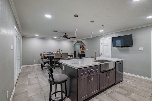 kitchen with light stone counters, ornamental molding, sink, hanging light fixtures, and an island with sink