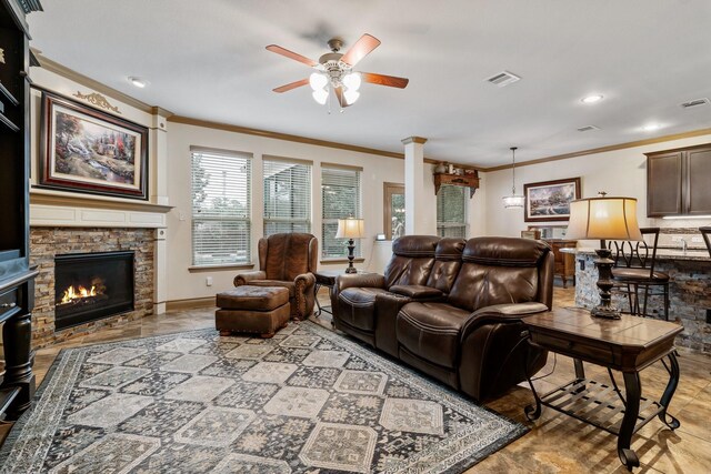 living room featuring a stone fireplace, ceiling fan, ornate columns, and ornamental molding