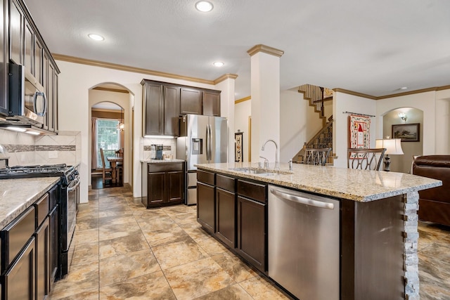 kitchen featuring appliances with stainless steel finishes, ornamental molding, dark brown cabinets, sink, and a center island with sink