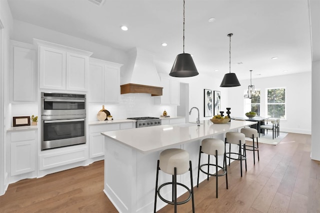 kitchen with a large island with sink, white cabinetry, stainless steel appliances, and custom exhaust hood