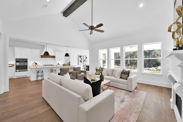 living room with beam ceiling, light hardwood / wood-style floors, high vaulted ceiling, and ceiling fan