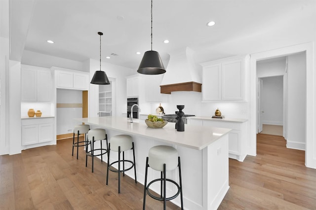 kitchen with a center island with sink, custom exhaust hood, and light wood-type flooring