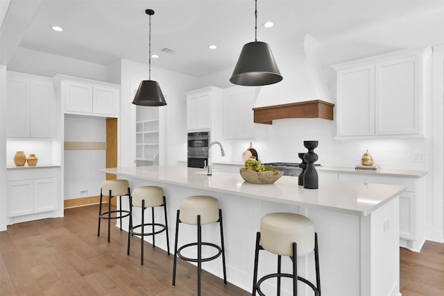 kitchen with white cabinetry, an island with sink, pendant lighting, and light wood-type flooring