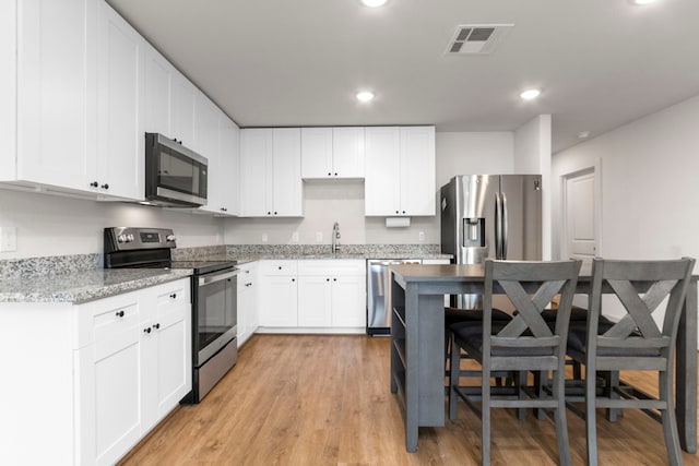 kitchen with light stone countertops, appliances with stainless steel finishes, light wood-type flooring, sink, and white cabinets