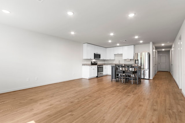 kitchen with white cabinetry, a kitchen breakfast bar, light hardwood / wood-style flooring, a kitchen island, and appliances with stainless steel finishes