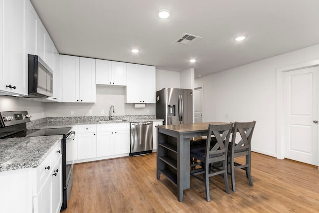 kitchen featuring white cabinets, sink, light wood-type flooring, light stone counters, and stainless steel appliances