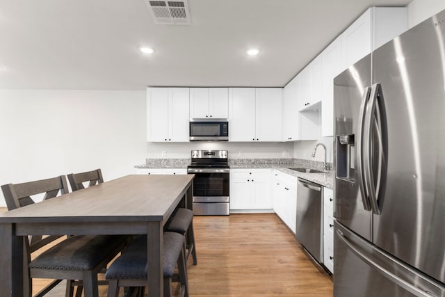 kitchen featuring white cabinetry, sink, stainless steel appliances, light stone counters, and light hardwood / wood-style floors