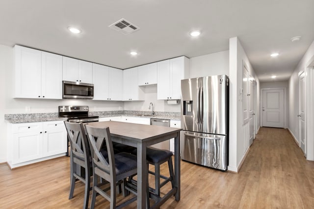 kitchen featuring sink, light wood-type flooring, appliances with stainless steel finishes, a kitchen bar, and white cabinetry