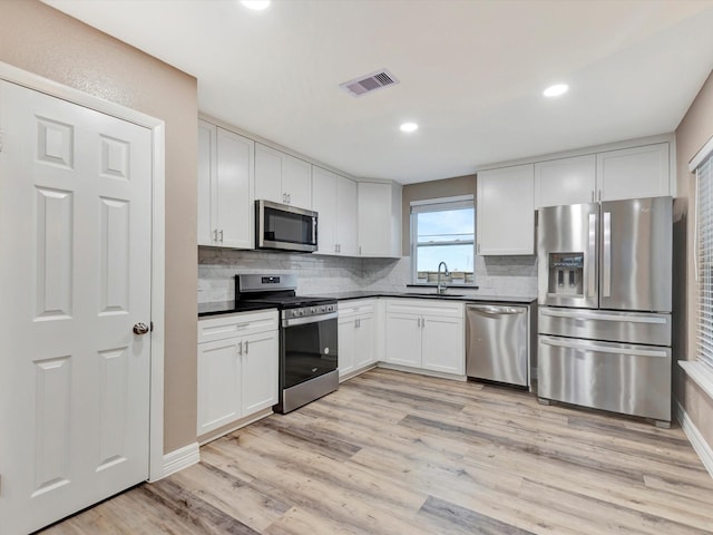 24 N Omega St, La Marque, TX 77568 - kitchen with decorative backsplash, appliances with stainless steel finishes, sink, white cabinets, and light hardwood / wood-style floors