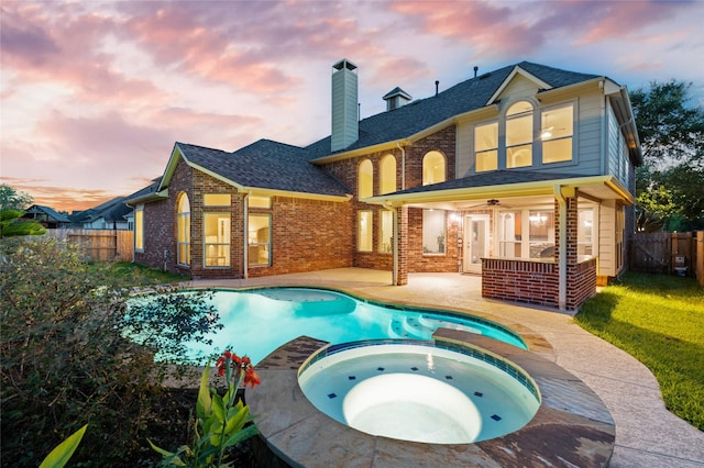 back house at dusk featuring ceiling fan, a patio area, and a pool with hot tub