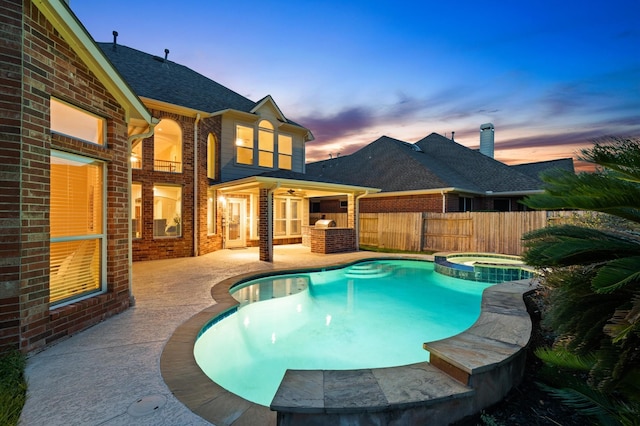 pool at dusk with ceiling fan, an in ground hot tub, and a patio