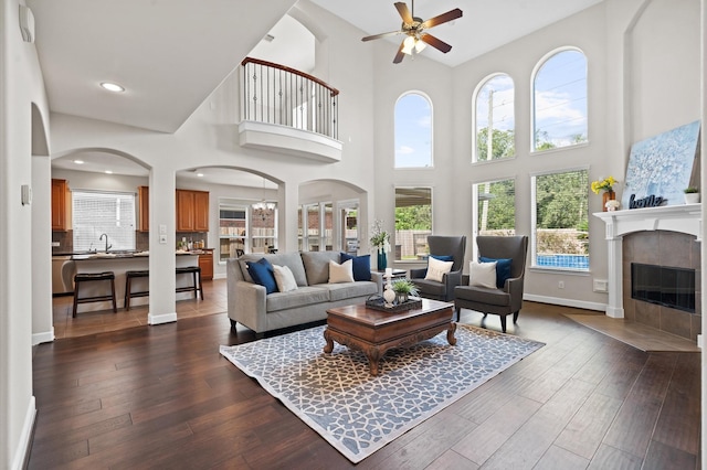 living room featuring sink, dark hardwood / wood-style floors, a towering ceiling, a fireplace, and ceiling fan with notable chandelier