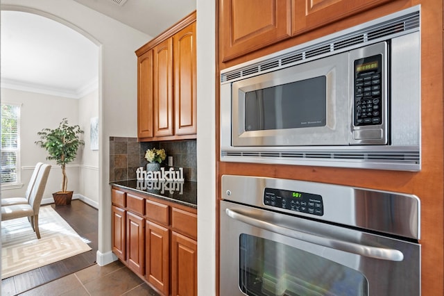 kitchen featuring dark hardwood / wood-style flooring, crown molding, appliances with stainless steel finishes, and tasteful backsplash