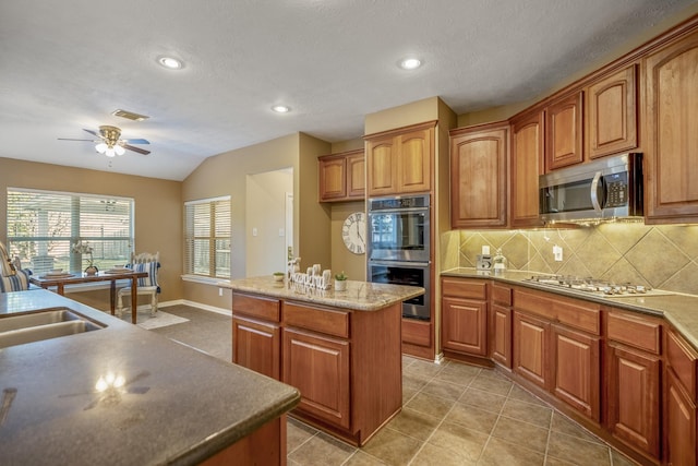 kitchen featuring sink, light tile patterned flooring, lofted ceiling, a kitchen island, and appliances with stainless steel finishes