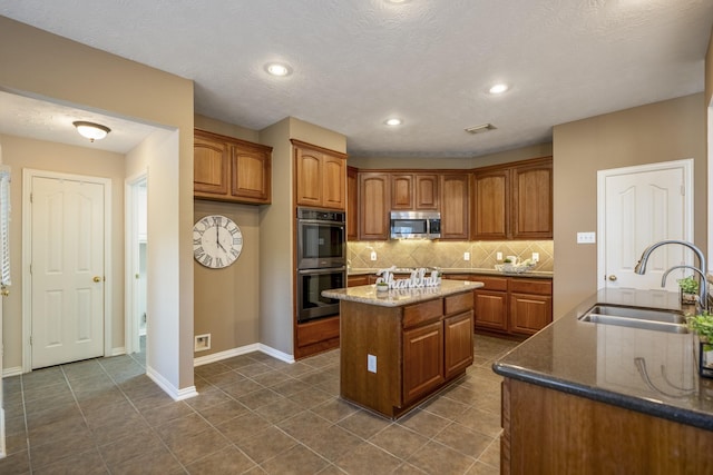 kitchen featuring a center island with sink, sink, dark stone countertops, tasteful backsplash, and stainless steel appliances