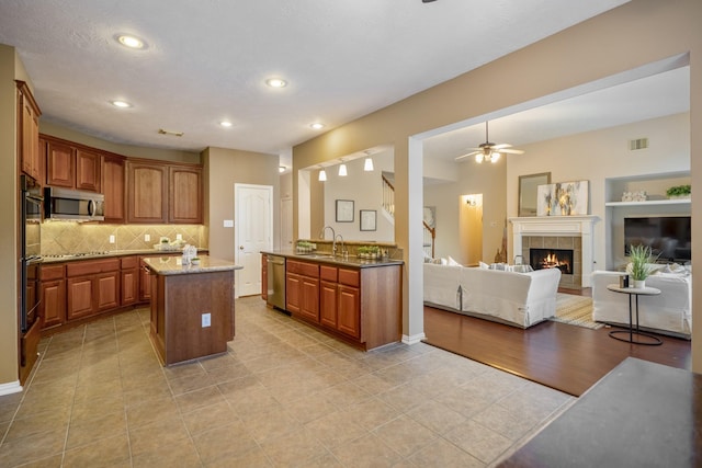 kitchen with sink, stainless steel appliances, backsplash, a tiled fireplace, and a kitchen island