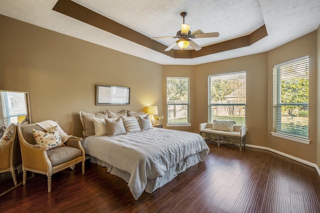 bedroom with a raised ceiling, ceiling fan, dark hardwood / wood-style flooring, and multiple windows