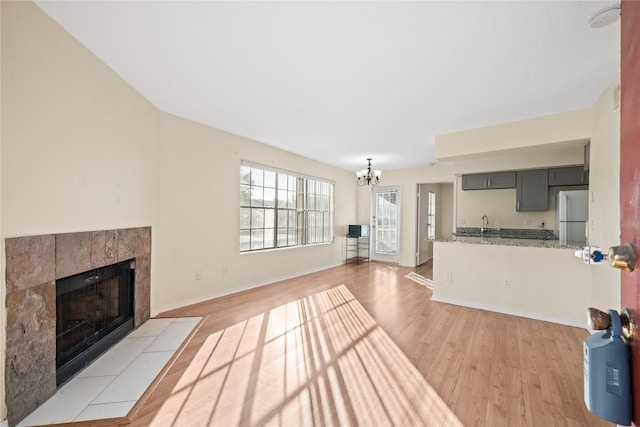 living room with a notable chandelier, light wood-type flooring, and a tiled fireplace