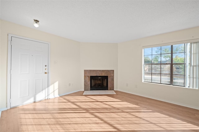 unfurnished living room with a tiled fireplace, a textured ceiling, and light wood-type flooring