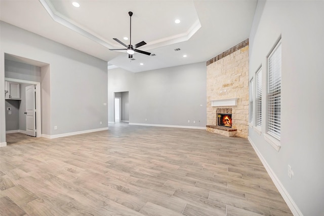 unfurnished living room with ceiling fan, light hardwood / wood-style floors, a stone fireplace, and a tray ceiling