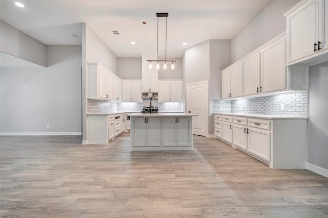 kitchen featuring a kitchen island with sink, decorative backsplash, light wood-type flooring, decorative light fixtures, and white cabinetry