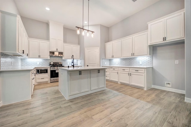 kitchen with a kitchen island with sink, white cabinets, stainless steel appliances, and light wood-type flooring