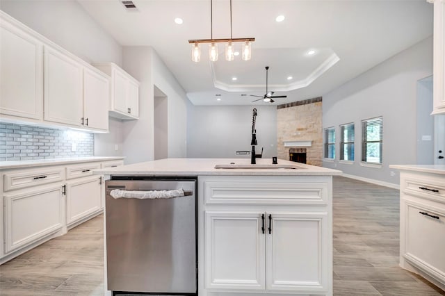 kitchen with stainless steel dishwasher, a tray ceiling, a fireplace, white cabinets, and a center island with sink