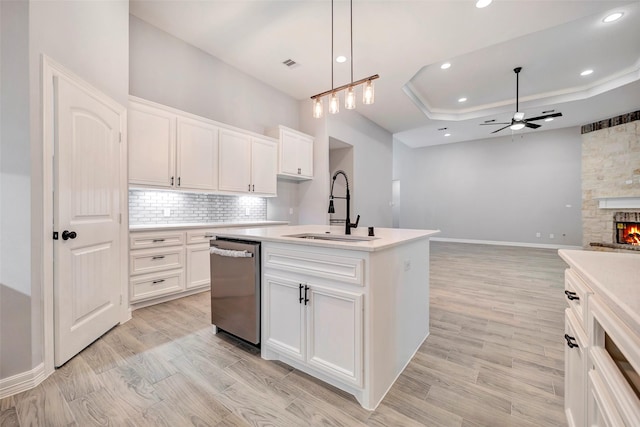 kitchen with decorative light fixtures, sink, white cabinetry, and an island with sink