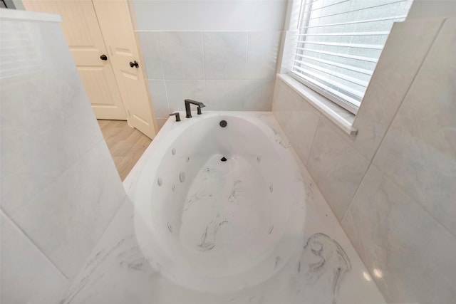 bathroom with a tub to relax in and tile walls