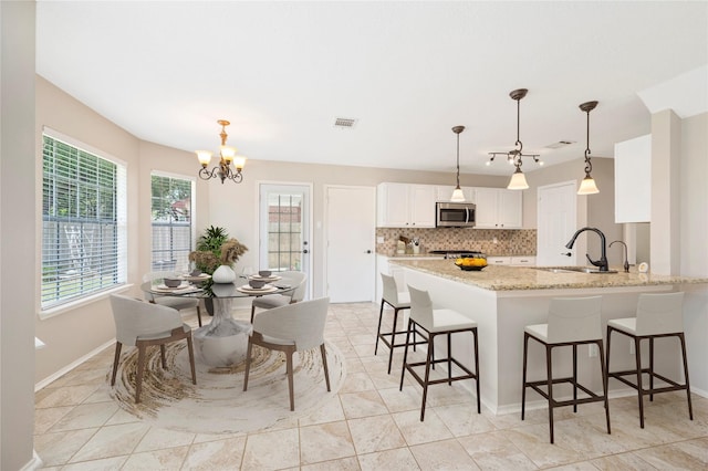 kitchen with white cabinetry, sink, stainless steel appliances, light stone counters, and pendant lighting