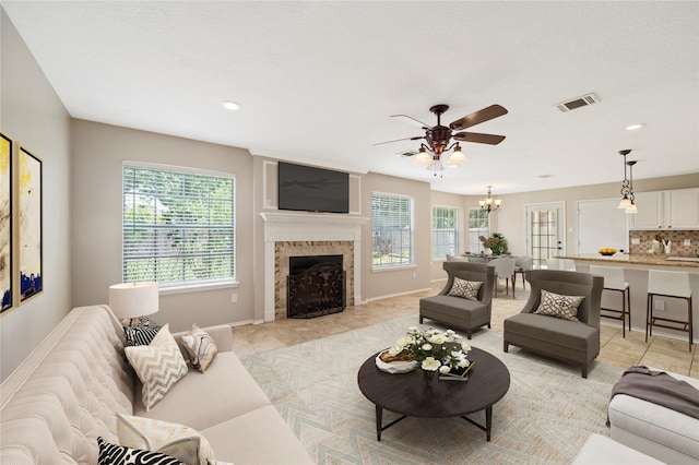 living room featuring a fireplace, light tile patterned floors, and ceiling fan with notable chandelier