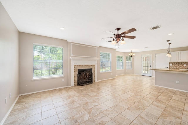 unfurnished living room featuring ceiling fan with notable chandelier, light tile patterned flooring, and a tiled fireplace