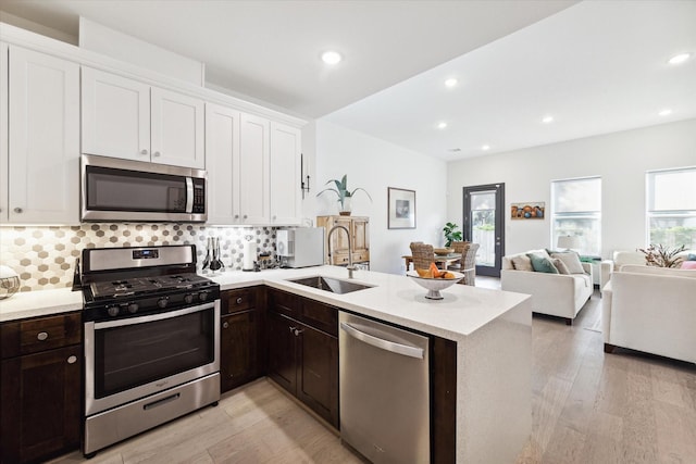 kitchen featuring sink, light hardwood / wood-style flooring, kitchen peninsula, white cabinets, and appliances with stainless steel finishes